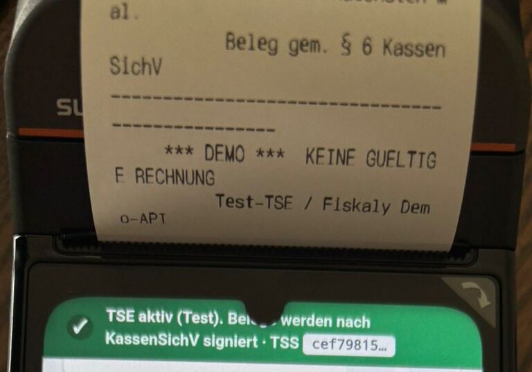 Foto, Ausschnitt: Testbon aus dem Drucker einer Sunmi V3h mit „Beleg gem. § 6 KassenSichV“, „*** DEMO *** keine gültige Rechnung“ und „Test-TSE / Fiskaly Demo-API“, darunter die Statuszeile der Quill-Kasse „TSE aktiv (Test)“